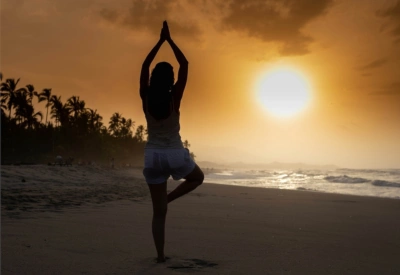 Kvinne som utøver yoga i oransje solnedgang på stranda.