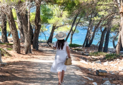 Kvinne går langs furuskogsti ved turkis hav på Lošinj i Kroatia – naturopplevelse langs Adriaterhavet