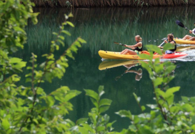 Damer som padler gul kajakk i grønt, speilblankt vann i Kroatia