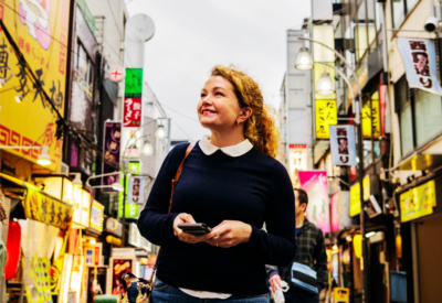 Smilende dame med krøllete hår som står i en travel gate i Tokyo.
