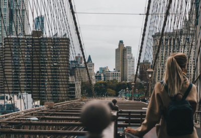 Kvinne på Brooklyn Bridge som står med ryggen til kamera og har på seg en ryggsekk. 