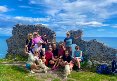 En glad gruppe kvinner sammen ved en steinformasjon foran utsikt til havet langs Amalfikysten. Foto.