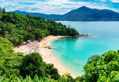 Bilde av en strand i Thailand. Turkist vann, gul sand og en frodig skog som omkranser stranden. Grønne åser i det fjerne.