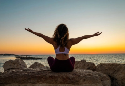 Dame som gjør yoga på strand i solnedgang. 