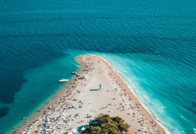 Den karakteristiske tuppen av stranda i Bol, som en trekant ut i havet. Havet er lyst turkis nærmest stranda og mørkere blågrønt lengre utover. Oversiktsbilde, mange små 'prikker' viser at det er folk på stranden. Foto.