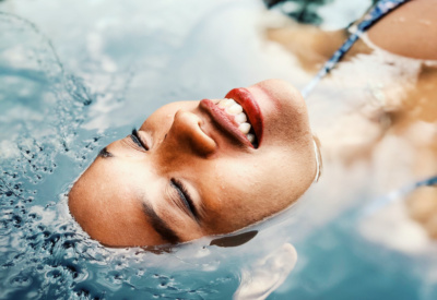 <p>Smilende kvinne med øynene lukket, flyter i varmt basseng.</p>