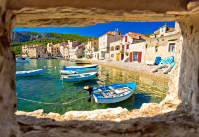 Innrammet bukt på øya vis i Kroatia. Fargerike båter, strand og murhus