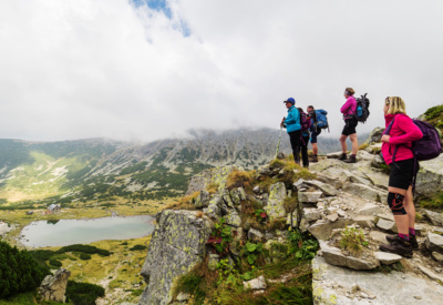 Fire personer i turklær og med ryggsekk står på en fjellkant og ser på utsikten over fjell og vann i Bulgaria. Foto.