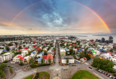 Oversiktsbilde over Reykjarvik med regnbue over hele byen og pastellfargede skyer. Foto.