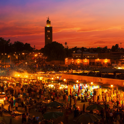 <p>Marrakech i Solnedgang. Moske i sort siluett og rød himmel i bakgrunn, markedsplass i front</p>