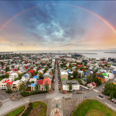 <p>Oversiktsbilde over Reykjarvik med regnbue over hele byen og pastellfargede skyer.</p>