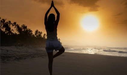 Kvinne som utøver yoga i oransje solnedgang på stranda.