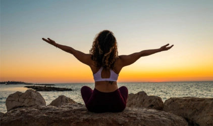 Dame som gjør yoga på strand i solnedgang. 