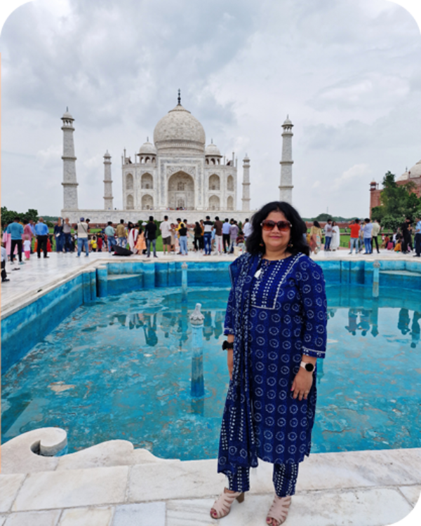 Et bilde av en Jyoti som står i tradisjonelle indisk blå drakt foran Taj Mahal i India.