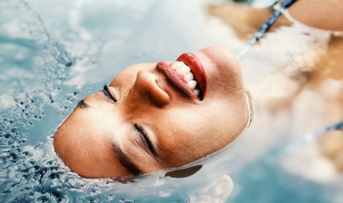 Smilende kvinne med øynene lukket, flyter i varmt basseng.