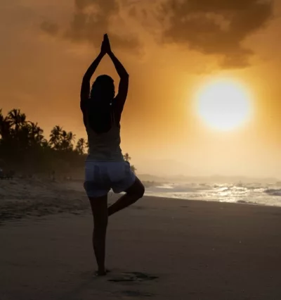 Kvinne som utøver yoga i oransje solnedgang på stranda.