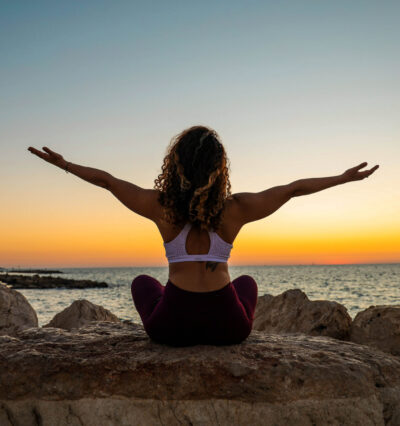 Dame som gjør yoga på strand i solnedgang. 