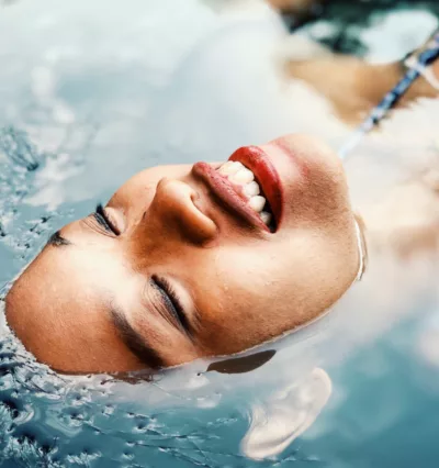 Smilende kvinne med øynene lukket, flyter i varmt basseng.