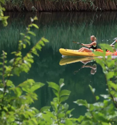 Damer som padler gul kajakk i grønt, speilblankt vann i Kroatia