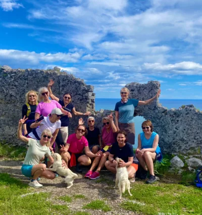 En glad gruppe kvinner sammen ved en steinformasjon foran utsikt til havet langs Amalfikysten. Foto.