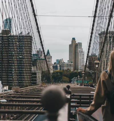 Kvinne på Brooklyn Bridge som står med ryggen til kamera og har på seg en ryggsekk. 